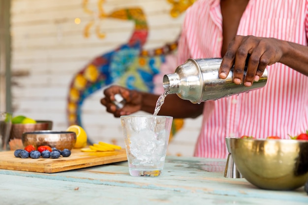 Midsection of biracial male bartender pouring cocktail from shaker at beach bar. Small business, work, refreshment, summer and vacation.