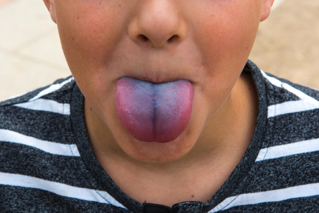 Photo midsection of boy sticking out tongue outdoors