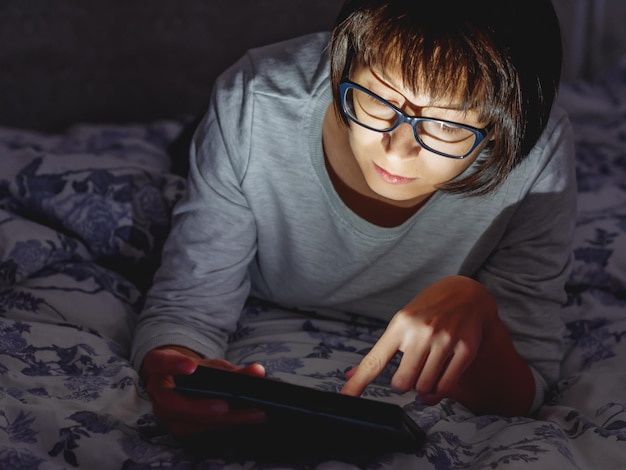 Photo midsection of boy using mobile phone on bed