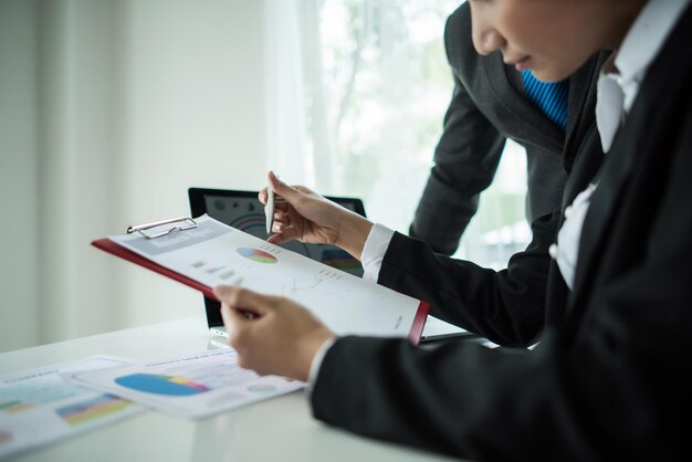 Midsection of business people analyzing chart on clipboard in office