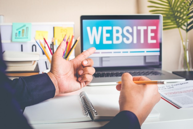 Photo midsection of business person holding pencil while pointing at laptop on table