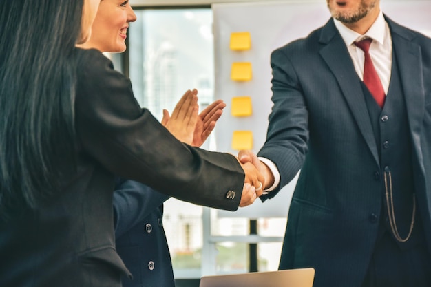Midsection of business person shaking hand while colleague clapping at office
