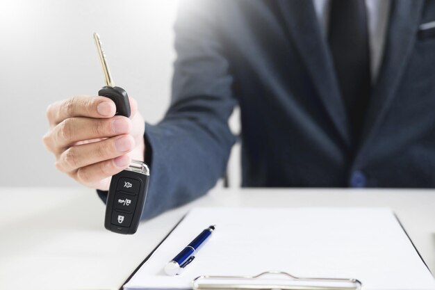 Foto sezione centrale di un uomo d'affari che tiene la chiave dell'auto con un documento sulla scrivania