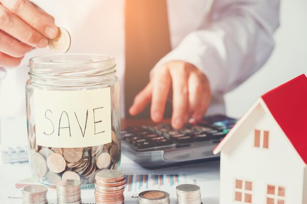 Midsection of businessman putting coin in jar on table