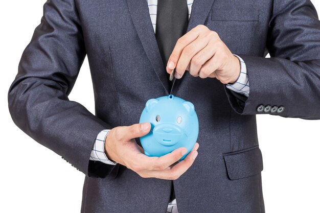 Midsection of businessman putting coin in piggy bank against white background