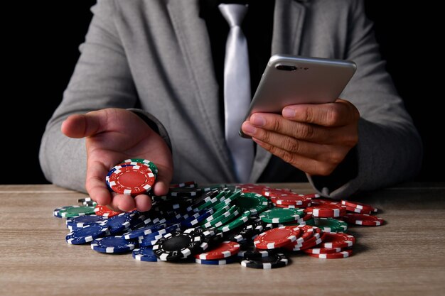Photo midsection of businessman with phone holding casino chips on desk