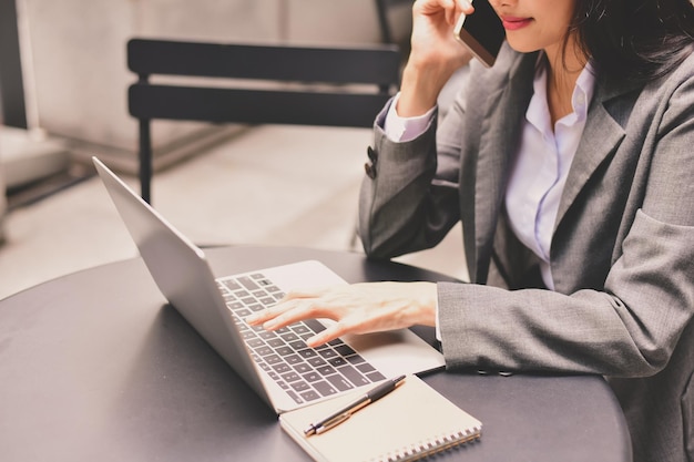 Midsection of businesswoman talking on mobile phone while using laptop at desk