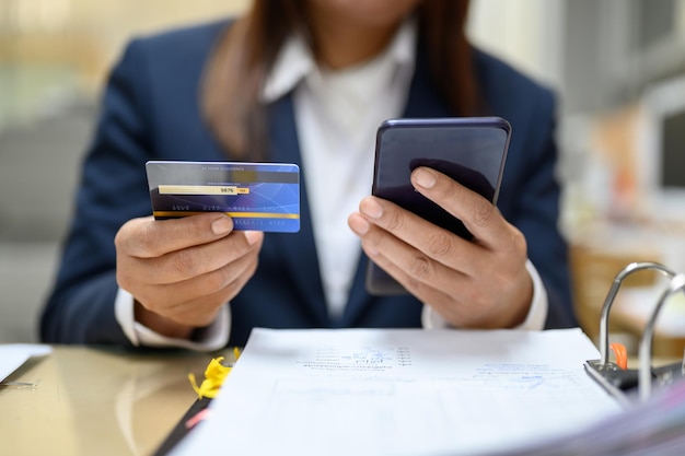 Foto sezione centrale di una donna d'affari che usa uno smartphone e una carta di credito sul tavolo