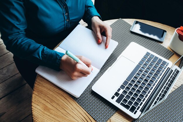 Midsection of businesswoman writing in book at office