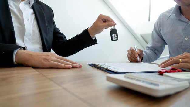 Midsection of car salesperson handing key on table