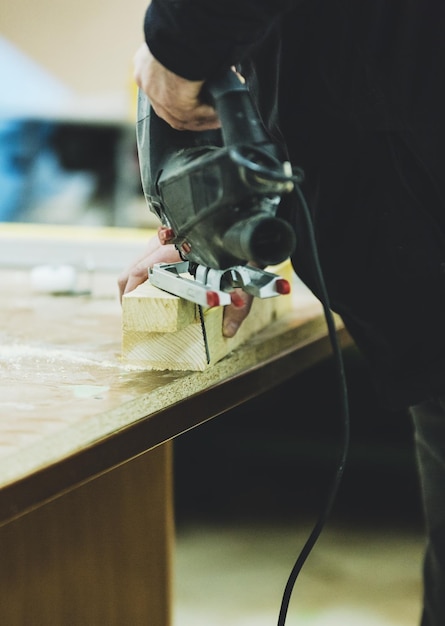 Midsection of carpenter drilling wood on table in workshop