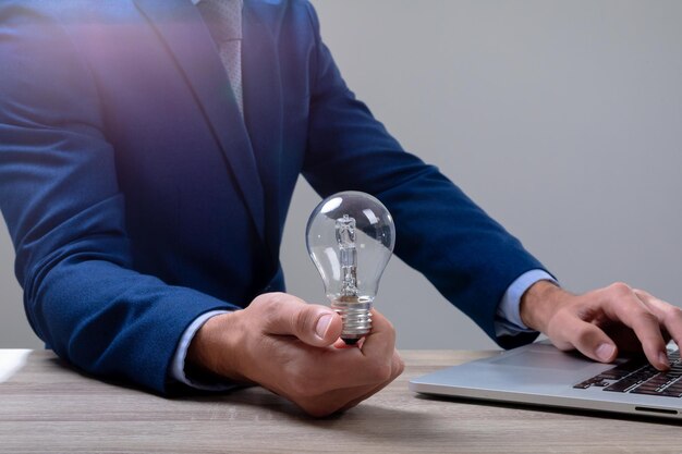 Midsection of caucasian businessman holding light bulb using laptop, isolated on grey background. business technology, communication and growth concept