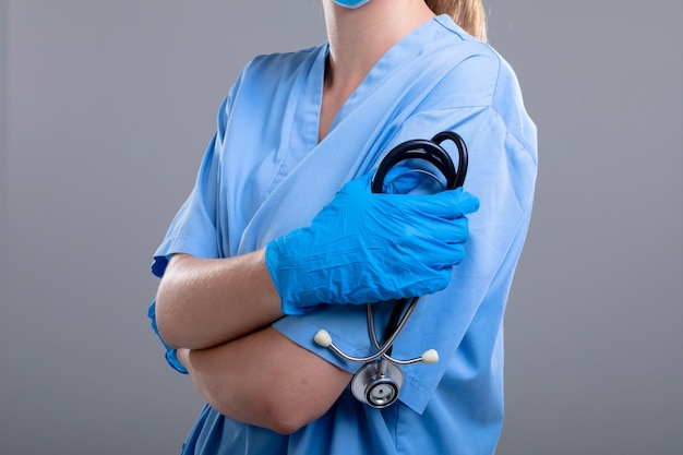 Photo midsection of caucasian female doctor holding stethoscope, isolated on grey background. medical and healthcare services concept.