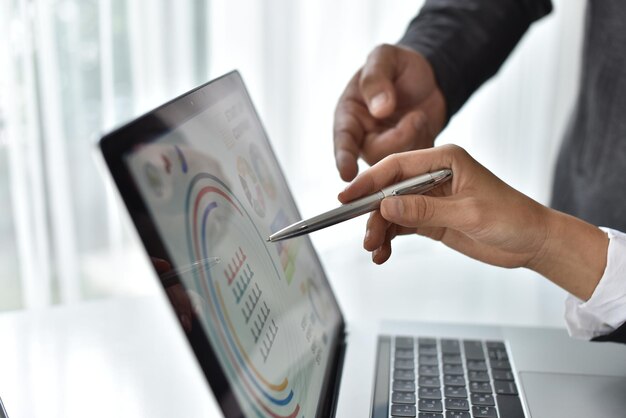 Midsection of colleagues analyzing charts on laptop in office