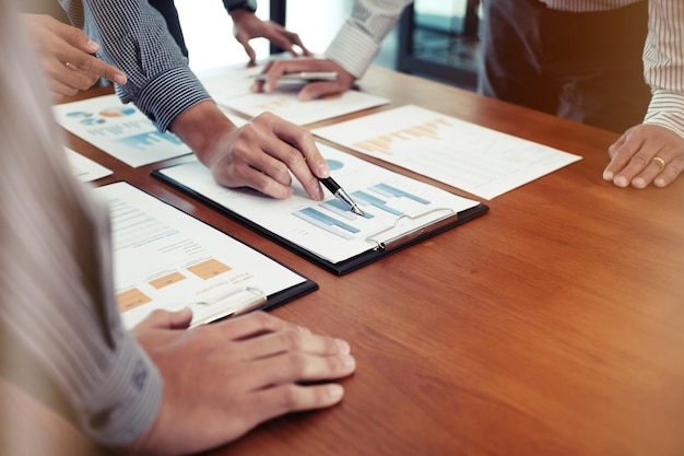 Midsection of colleagues analyzing charts on office desk