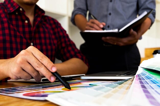 Photo midsection of colleagues discussing color swatch on desk in office