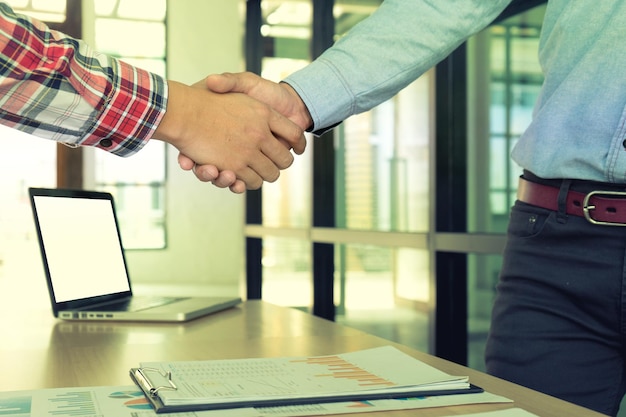 Midsection of colleagues shaking hands while standing in of office