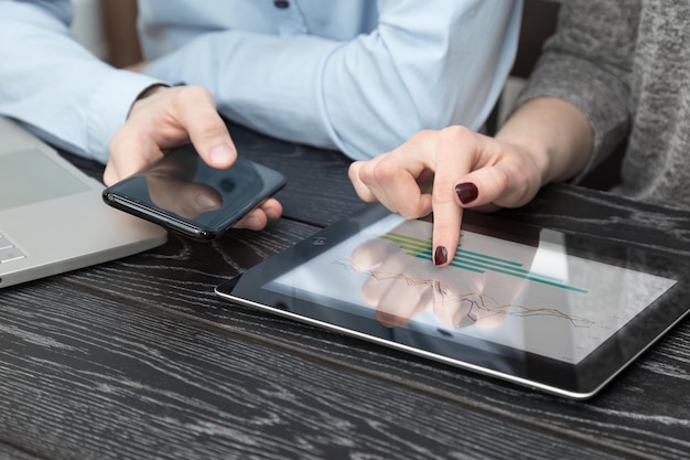 Photo midsection of colleagues using phones and digital tablet by laptop on desk