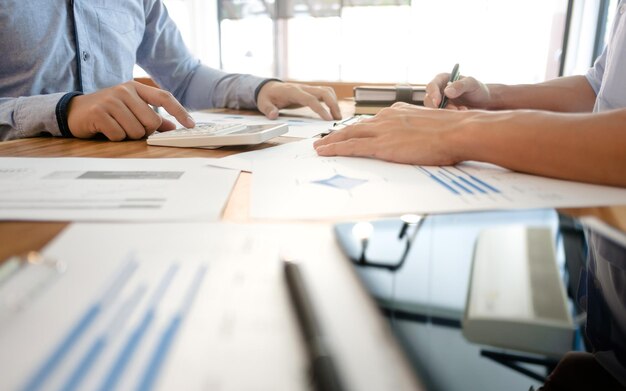 Midsection of colleagues with calculator analyzing chart on desk