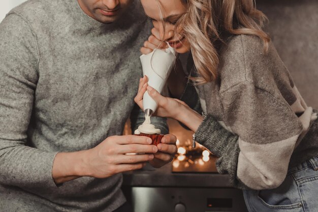 Midsection of couple decorating cupcake at home