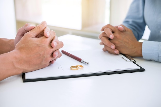 Photo midsection of couple sitting with divorce paper and rings on desk in courtroom