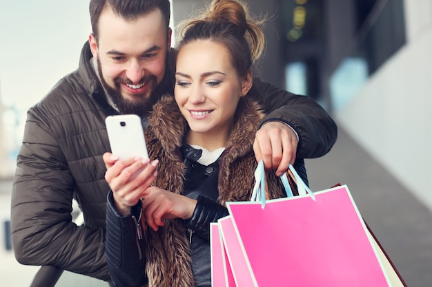 Midsection of couple with shopping bags and smartphone in city