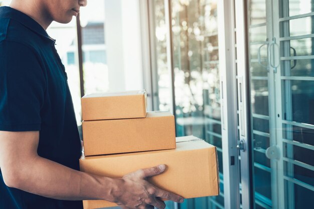 Midsection of delivery man holding cardboard boxes against house