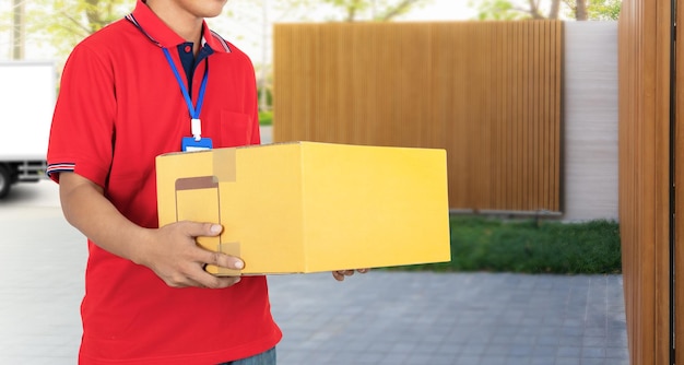 Midsection of delivery person holding cardboard box while standing outside house