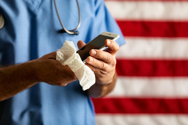 Midsection of doctor cleaning mobile phone with tissue paper