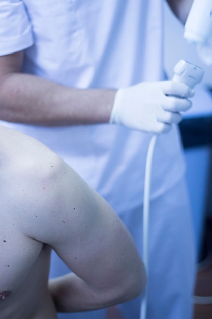 Midsection of doctor examining shirtless patient in hospital