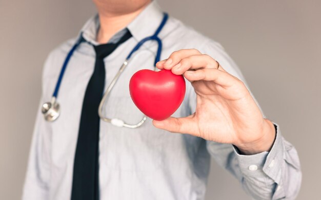 Photo midsection of doctor holding red heart shape against beige background