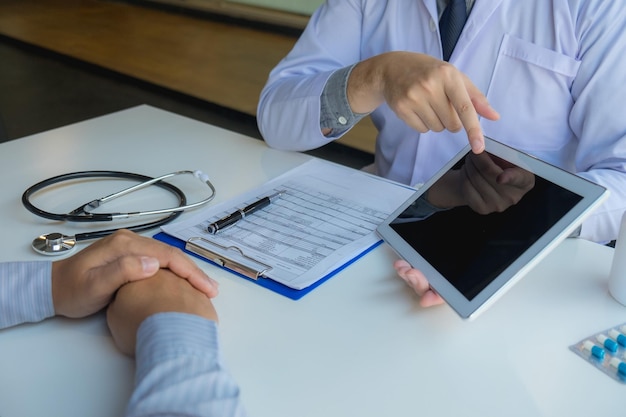 Photo midsection of doctor showing digital tablet to patient at clinic