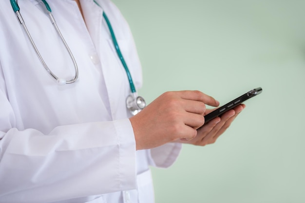 Midsection of doctor using smart phone against wall