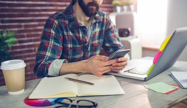 Midsection of editor using smartphone while working in office