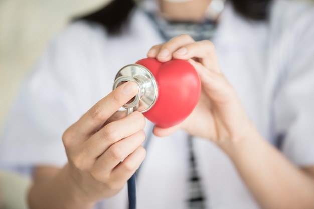 Midsection of female doctor analyzing red heart shape stress ball with stethoscope