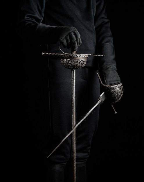 Photo midsection of a fencing master holding a 17th century sword and dagger against black background