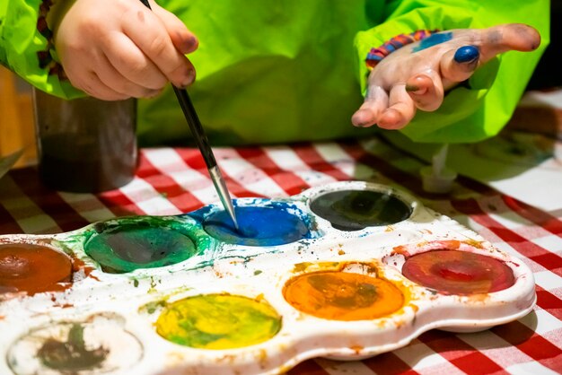 Photo midsection of girl holding paintbrush in paints on table