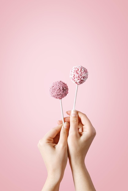Midsection of hand holding lollipops against pink background