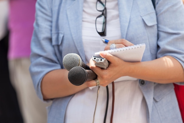 midsection of journalist writing in notepad while holding microphones