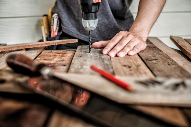 Midsection of male carpenter drilling wood in workshop