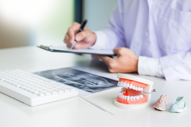 Foto sezione centrale di un dentista maschio che scrive su un documento con le dentiere dentali alla scrivania in ospedale