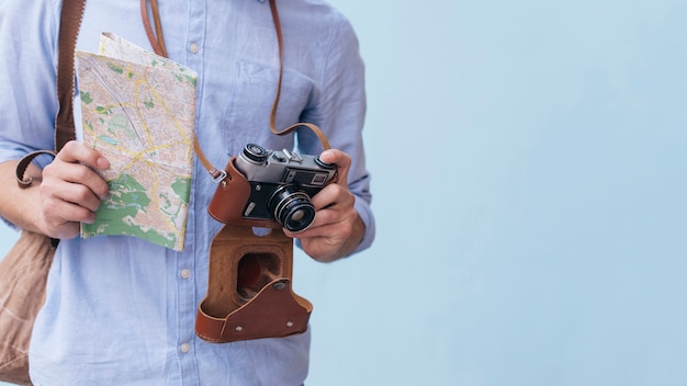 Midsection of male traveler photographer holding camera and map standing against blue background