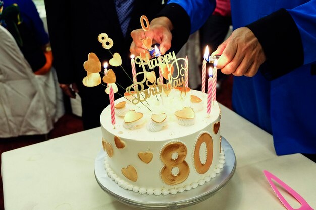 Photo midsection of man burning birthday candles on cake at table