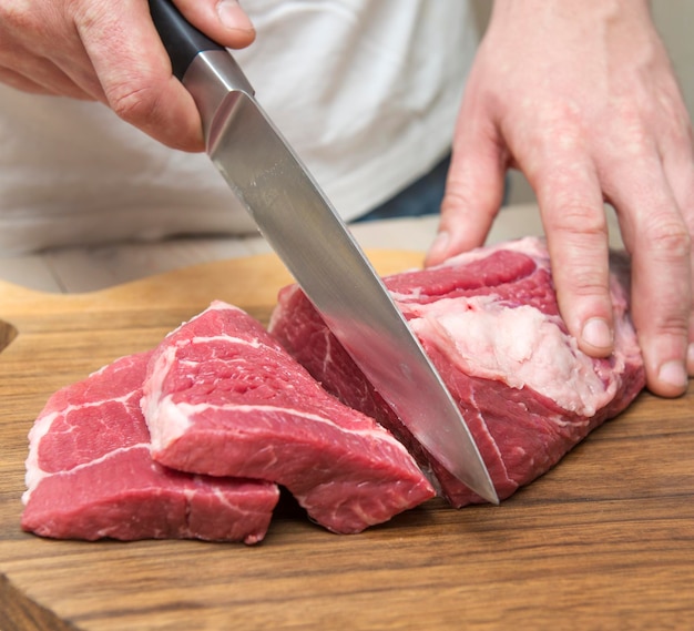 Midsection of man cutting meat on board