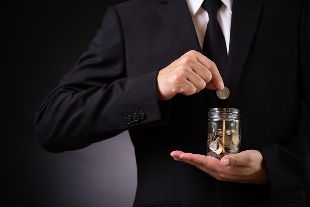 Photo midsection of man holding coin over jar against black background