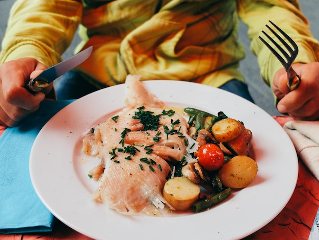 Photo midsection of man holding cutlery while sitting with food in plate at dining table