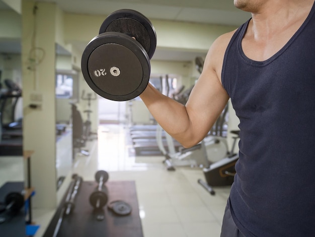 Photo midsection of man holding dumbbell while exercising in gym