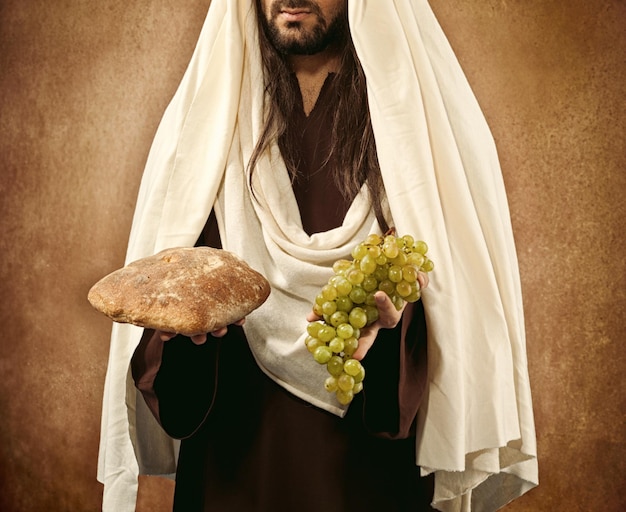 Photo midsection of man holding grapes and bread while standing against wall