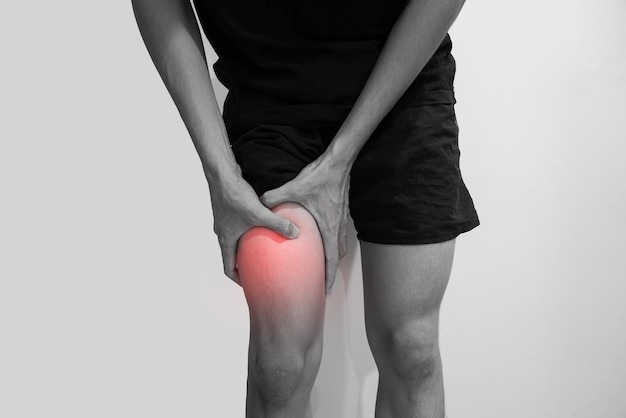 midsection of man holding leg in pain against white background