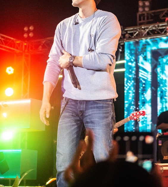 Midsection of man holding microphone while standing on stage at night